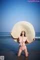 A woman in a pink bikini and a straw hat on the beach.