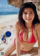 A woman in a red bikini sitting on a beach.